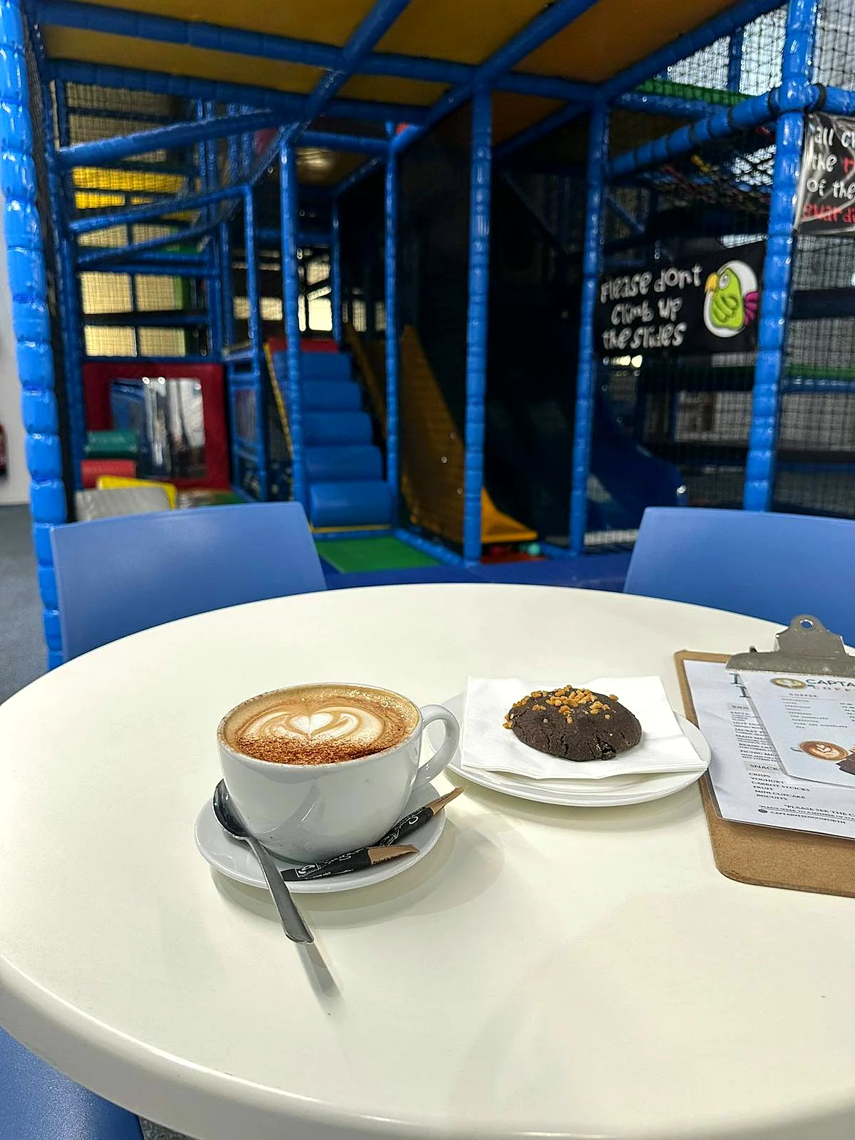 Cappuccino and a cookie on a café table beside the play frame